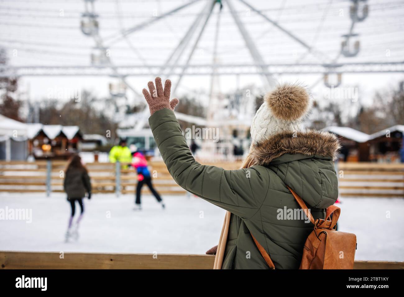 La femme fait signe à la foule de gens qui patinent sur la patinoire. Marché de Noël et vacances de l'Avent en ville. Sport d'hiver Banque D'Images