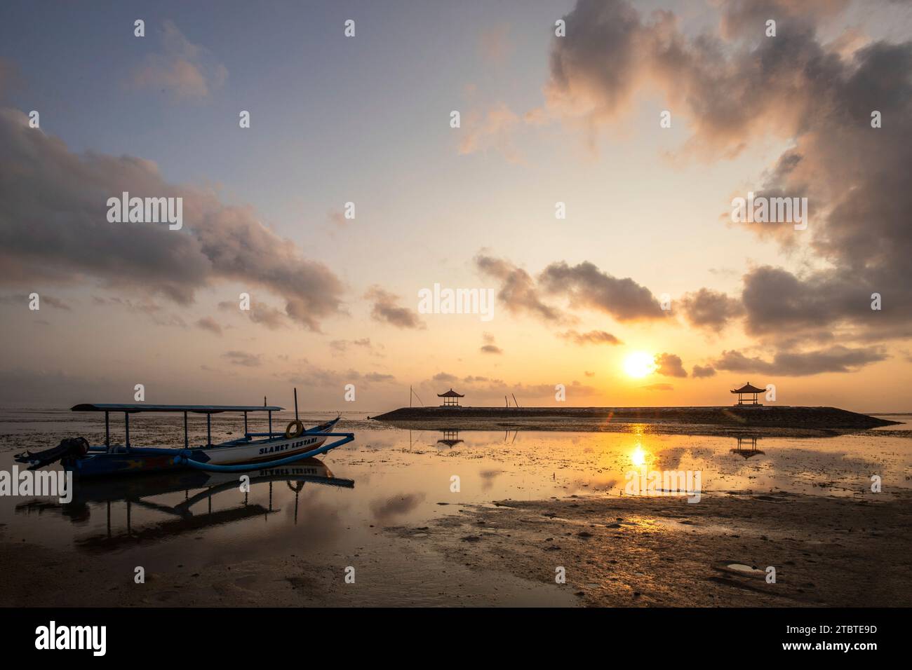 Paysage matinal pris sur une plage de sable, vue sur la mer à l'horizon avec de petits temples dans l'eau et un jukung, un bateau de pêche traditionnel, sur la plage, lever du soleil à Sanur, Bali, Indonésie Banque D'Images