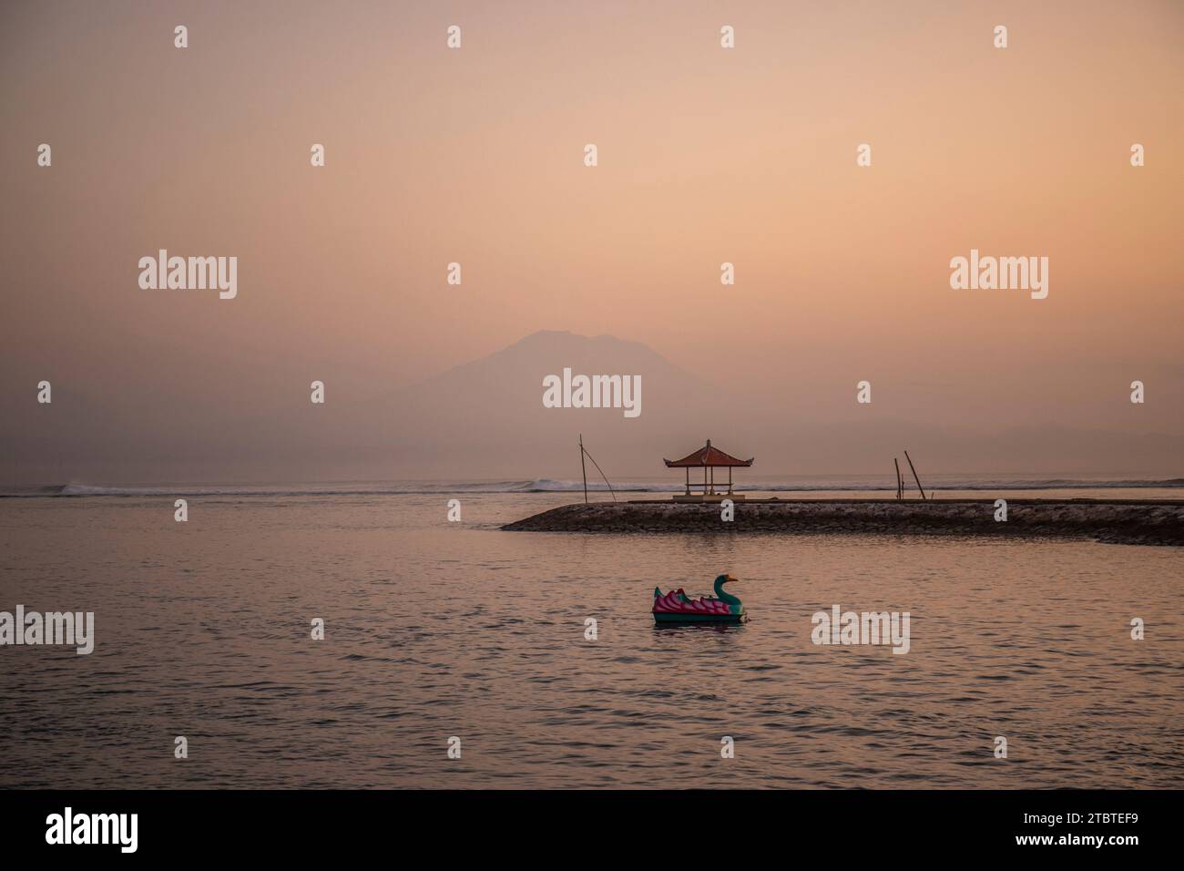 Lever du soleil sur la mer, vue de la plage de sable à l'horizon, dans la mer il y a des brise-lames avec de petits temples, eau calme avec de petites vagues et reflets sur la plage tropicale de Sanur, Bali, Indonésie Banque D'Images