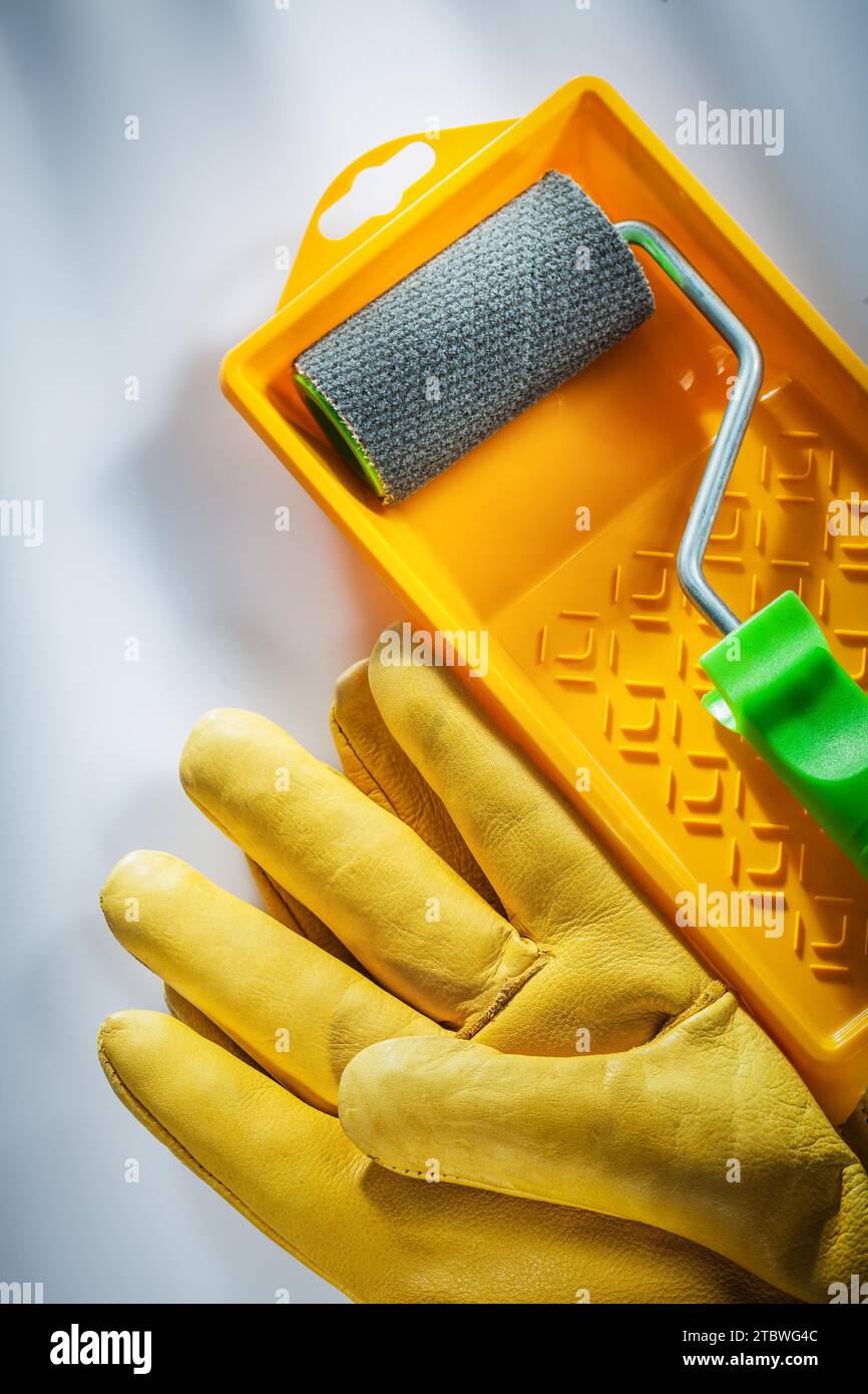 Gants de protection jaunes rouleau de bac à peinture sur surface blanche Banque D'Images
