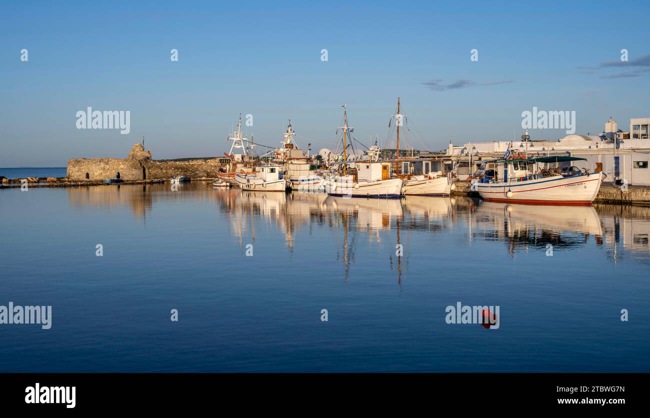 Bateaux de pêche dans le port et les ruines du château vénitien, reflétés dans la mer, au coucher du soleil, Naoussa, Paros, Cyclades, Grèce Banque D'Images