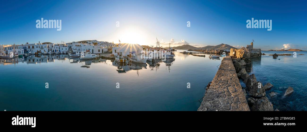 Panorama, bateaux de pêche dans le port de Naoussa au coucher du soleil, reflété dans la mer, étoile du soleil, ruines du château vénitien sur la droite, blanc Banque D'Images