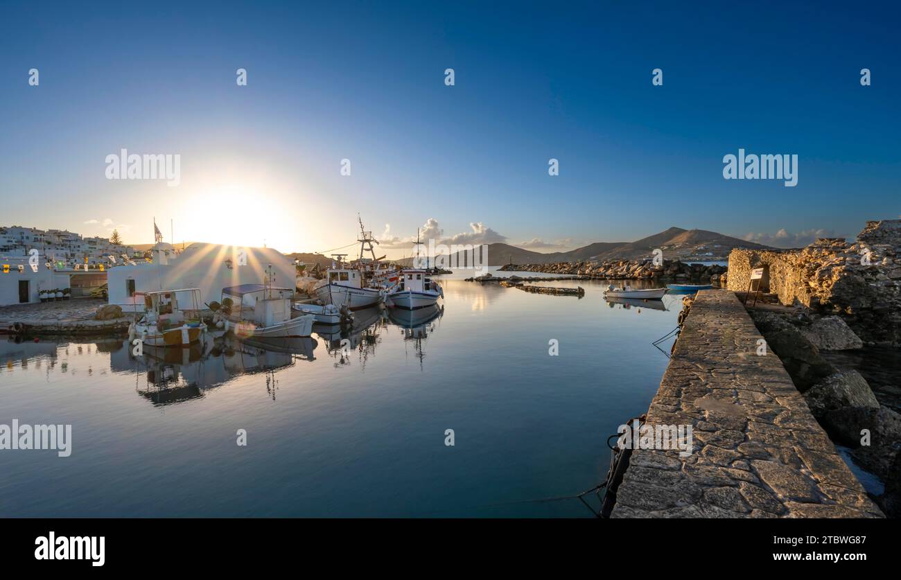 Bateaux de pêche dans le port de Naoussa au coucher du soleil, reflétés dans la mer, étoile du soleil, ruines du château vénitien sur la droite, maisons blanches des Cyclades Banque D'Images