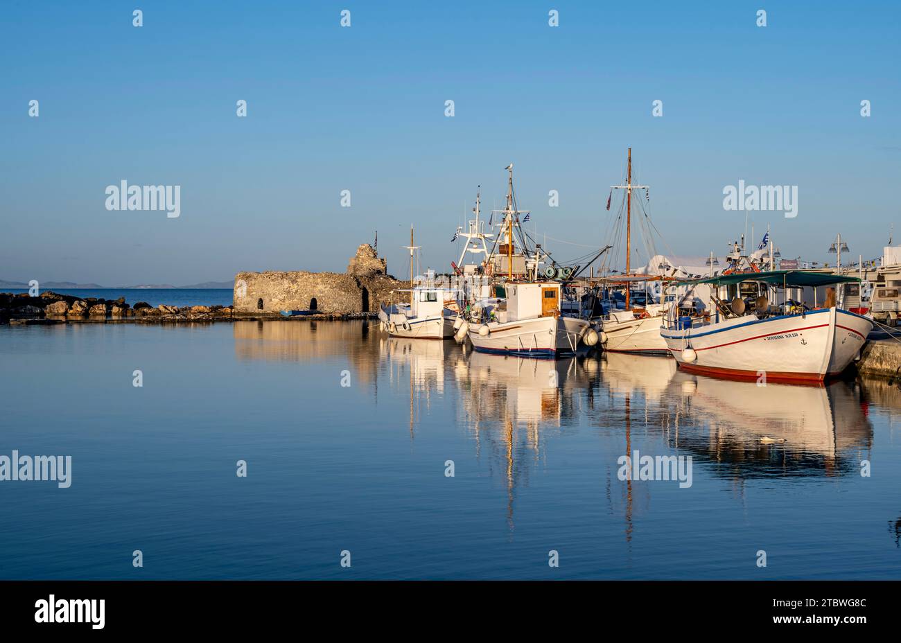 Bateaux de pêche dans le port et les ruines du château vénitien, reflétés dans la mer, au coucher du soleil, Naoussa, Paros, Cyclades, Grèce Banque D'Images