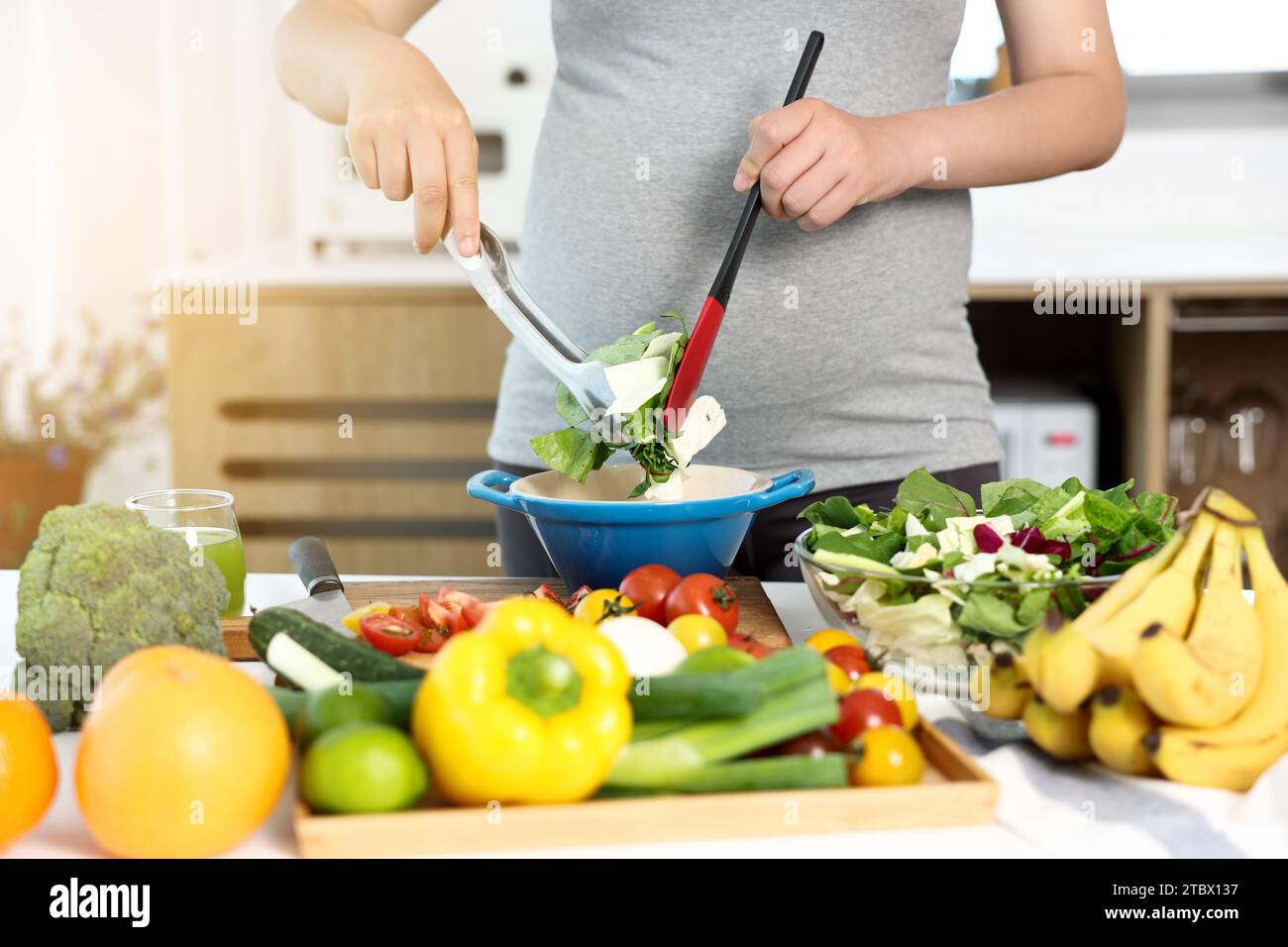 Une femme enceinte prépare un plat de salade à table Banque D'Images