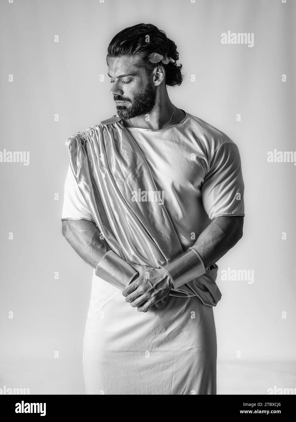 Un homme musclé avec une barbe portant une écharpe jaune et une robe blanche, dans un costume de dieu grec ou romain, en studio Banque D'Images