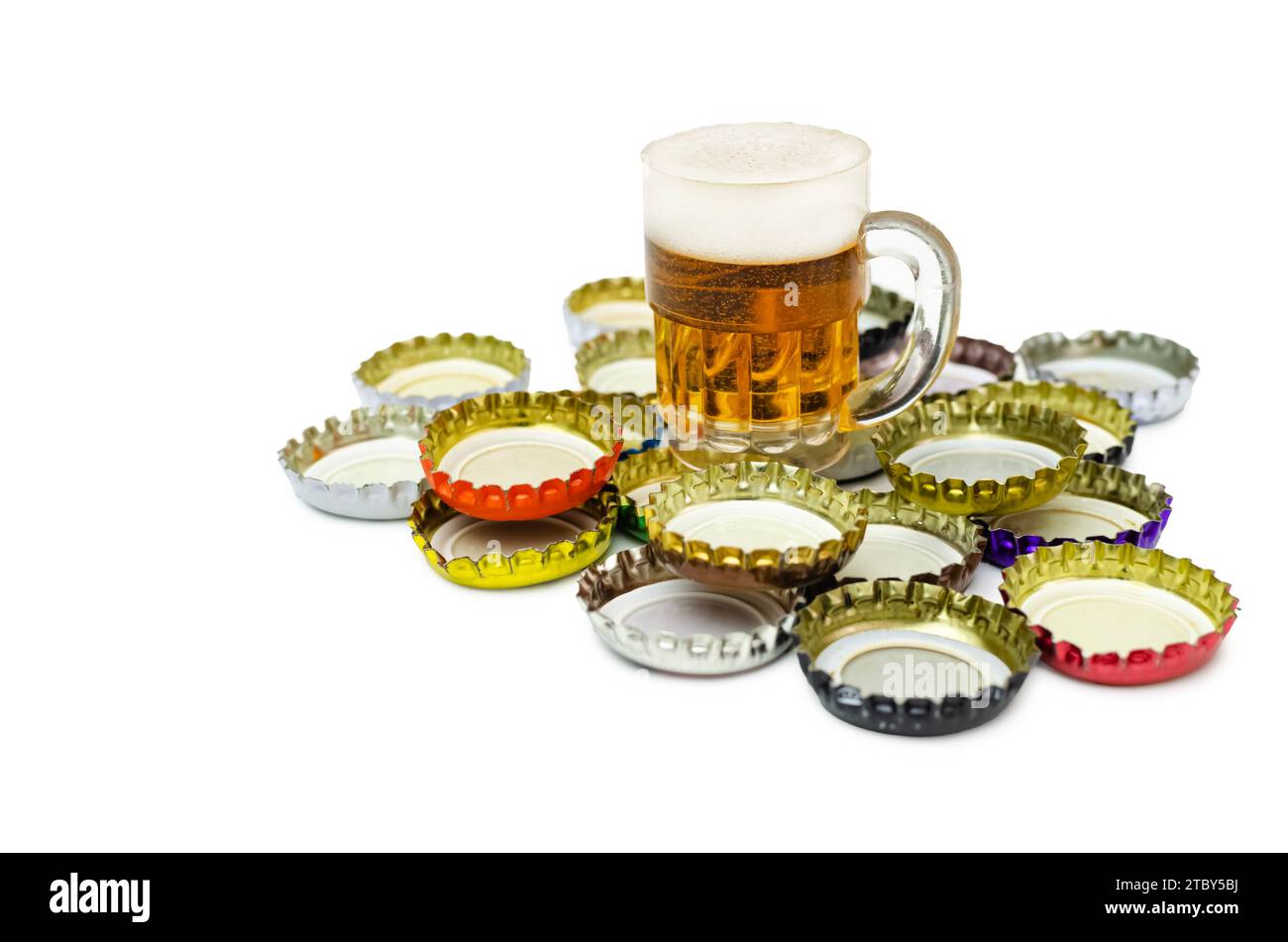 Bouchons de bouteille de bière en métal couronnent le groupe isolé sur blanc. Sur le dessus est une tasse de bière décorative. Image conceptuelle de la consommation d'alcool. Banque D'Images