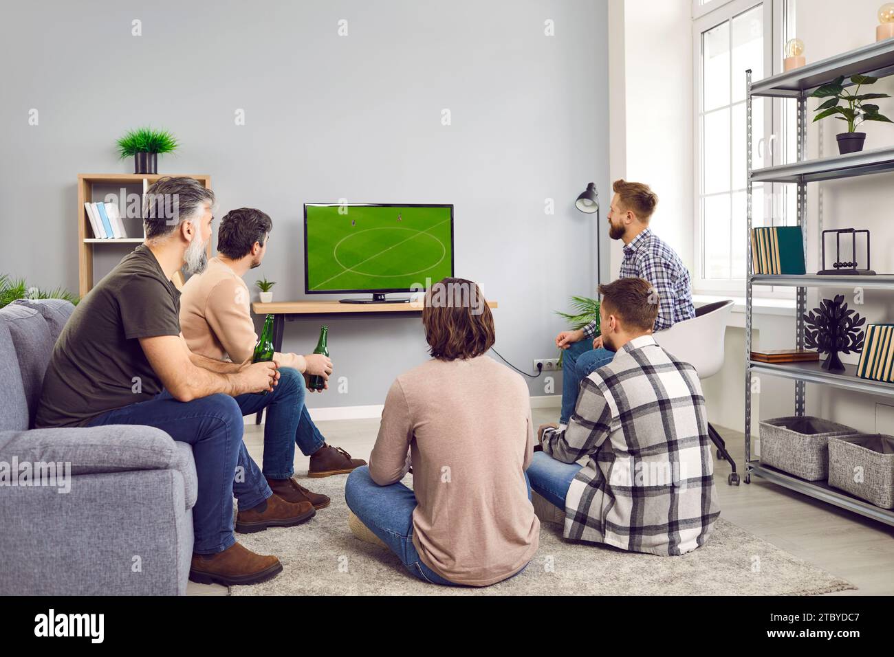 Groupe d'amis barbus matures regardant un match de football à la télévision à la maison avec de la bière. Banque D'Images