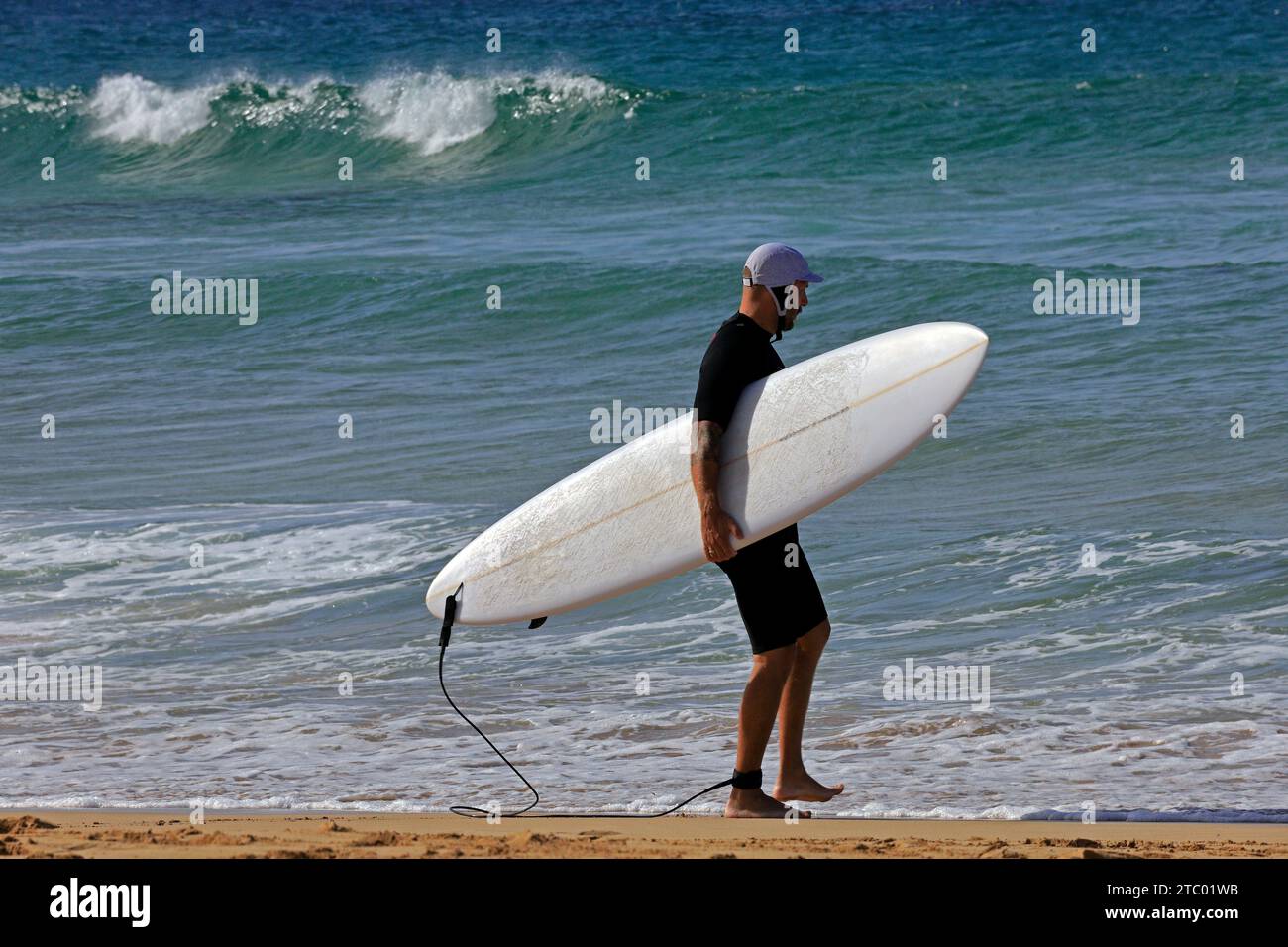 Homme portant planche de surf marchant vers la mer et testant l'eau avec les orteils, El Cotillo, Fuerteventura, Îles Canaries, Espagne. Prise en novembre 2023 Banque D'Images
