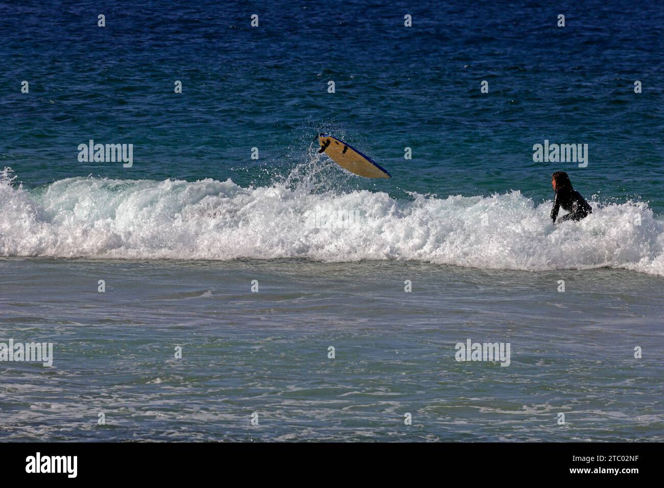 Surfer disparaît sous une vague tandis que sur board décolle. Surf à Piedra Beach, El Cotillo, Fuerteventura, Îles Canaries, Espagne. Prise en novembre 2023 Banque D'Images