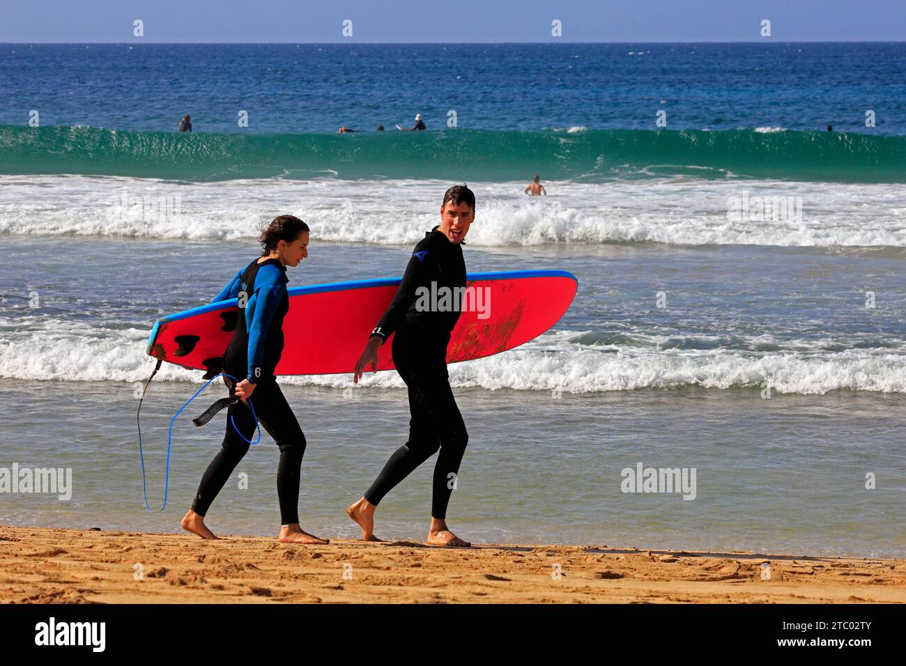 Homme et femme partageant une planche de surf marchant ensemble à Piedra Beach, El Cotillo, Fuerteventura, Îles Canaries, Espagne. Prise en novembre 2023 Banque D'Images