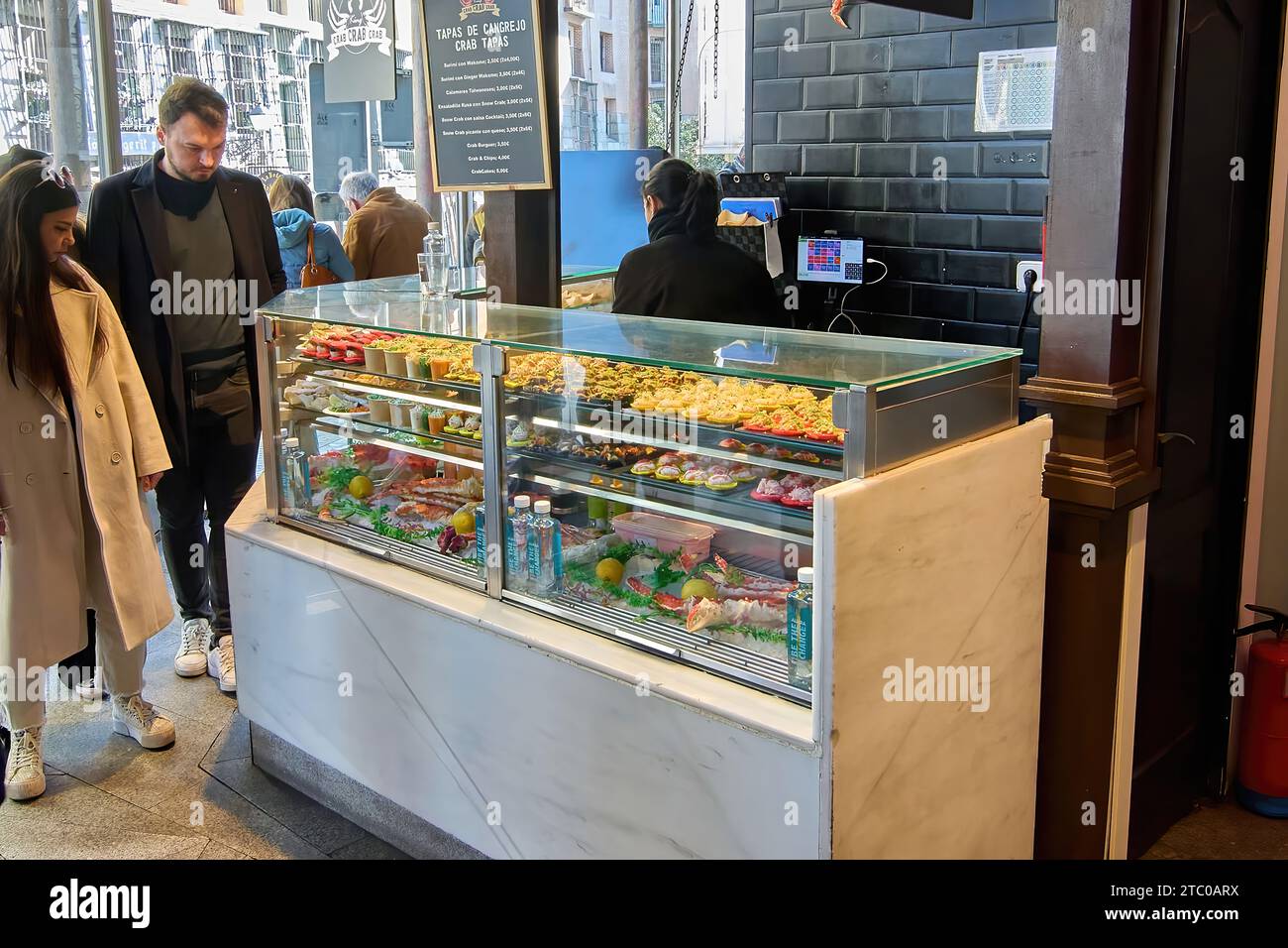 MADRID ESPAGNE - 09 DÉCEMBRE 2023 : Jeune couple regardant des tapas dans une entreprise du marché de Sant Miguel à base de crabe. Banque D'Images