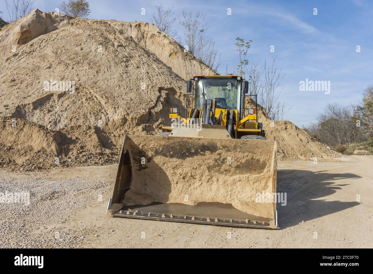 Une excavatrice s'est arrêtée dans une aire de travail avec une montagne de sable et de gravier sur le sol Banque D'Images