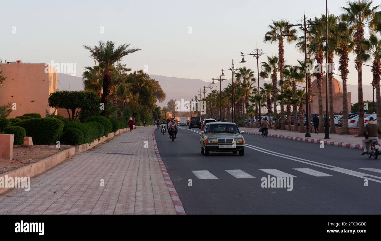 Trafic au coucher du soleil le long d'une route bordée de palmiers à l'extérieur des murs de la médina gauche dans la ville de Marrakech aka Marrakech, Maroc, 09 décembre 2023 Banque D'Images