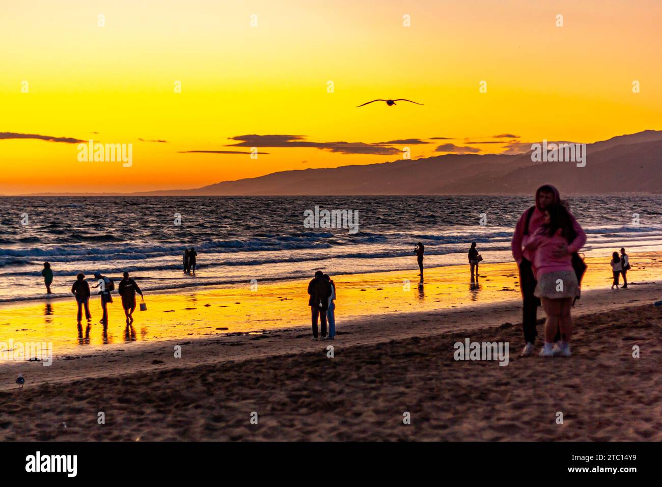 Les touristes se sont silhouettés sur la plage de Santa Monica au coucher du soleil dans le sud de la Californie, reflétés dans l'eau par les vagues de l'océan Banque D'Images