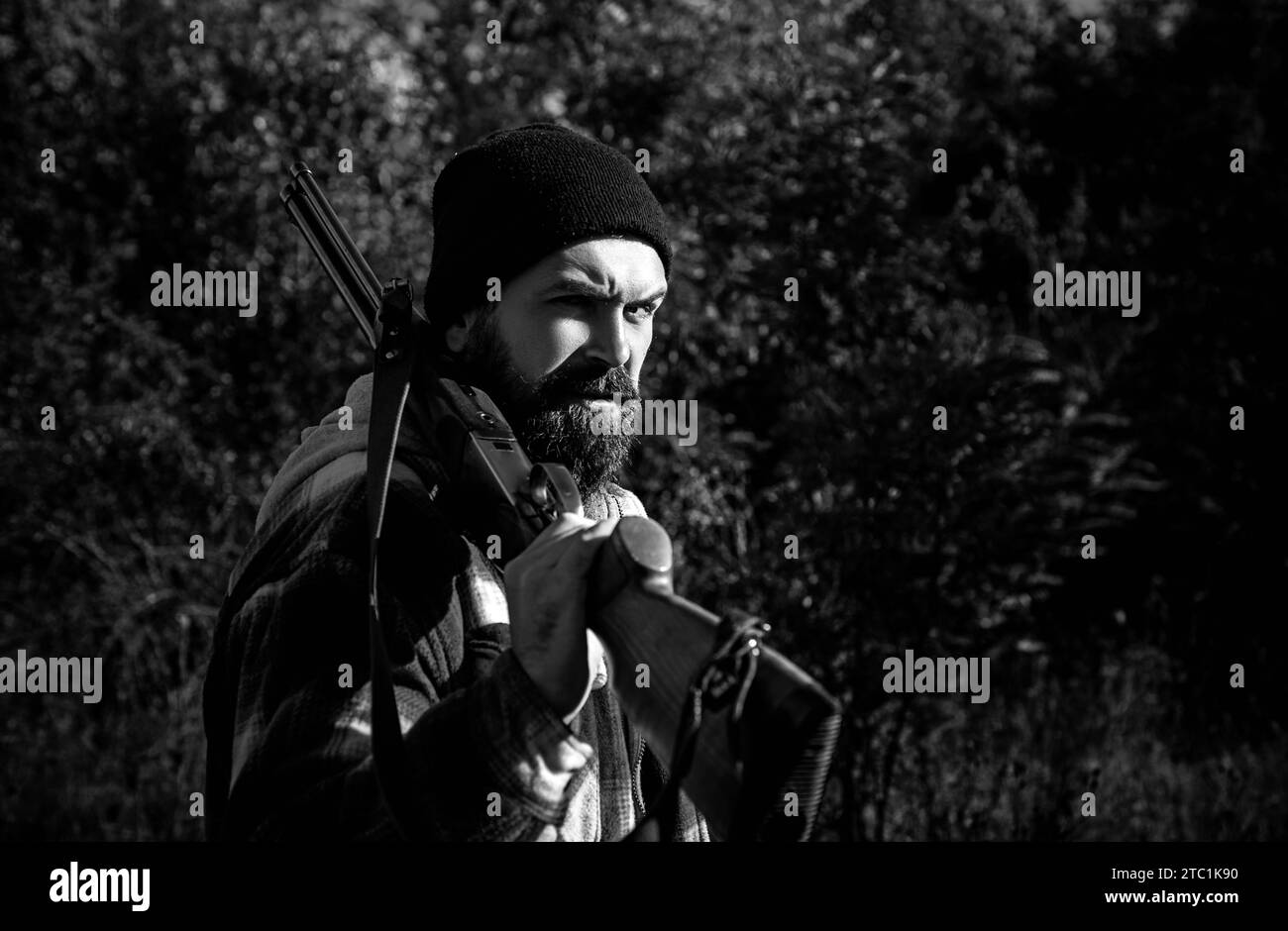 Chasseur barbu tenant le fusil et marchant dans la forêt. Chasseur avec fusil de chasse. Banque D'Images