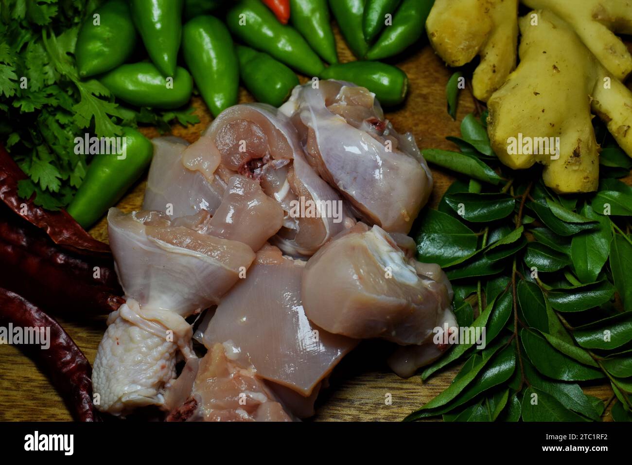 Ail frais, oignon, vert piment, poulet cru, gingembre, feuilles de coriandre et feuilles de curry sur plateau en bois avec de l'eau saupoudrée sur ces légumes. Banque D'Images