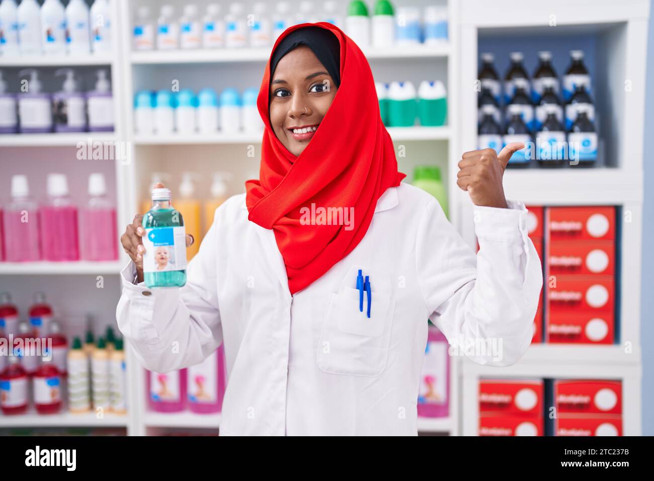 Jeune femme arabe travaillant à la pharmacie pharmacie tenant le sirop pointant le pouce vers le haut sur le côté souriant heureux avec la bouche ouverte Banque D'Images