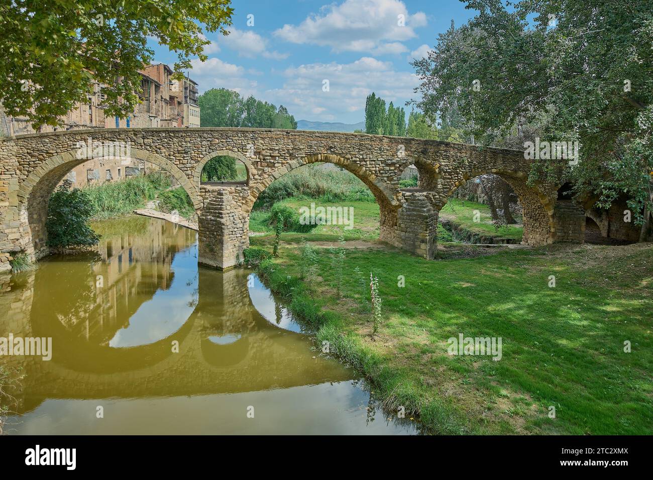 Pont Queralt sur la rivière Meder, 11e siècle, Vic, Osona, Barcelone, Catalogne, Espagne avec des eaux calmes et des prairies verdoyantes avec un ciel bleu avec CLO Banque D'Images