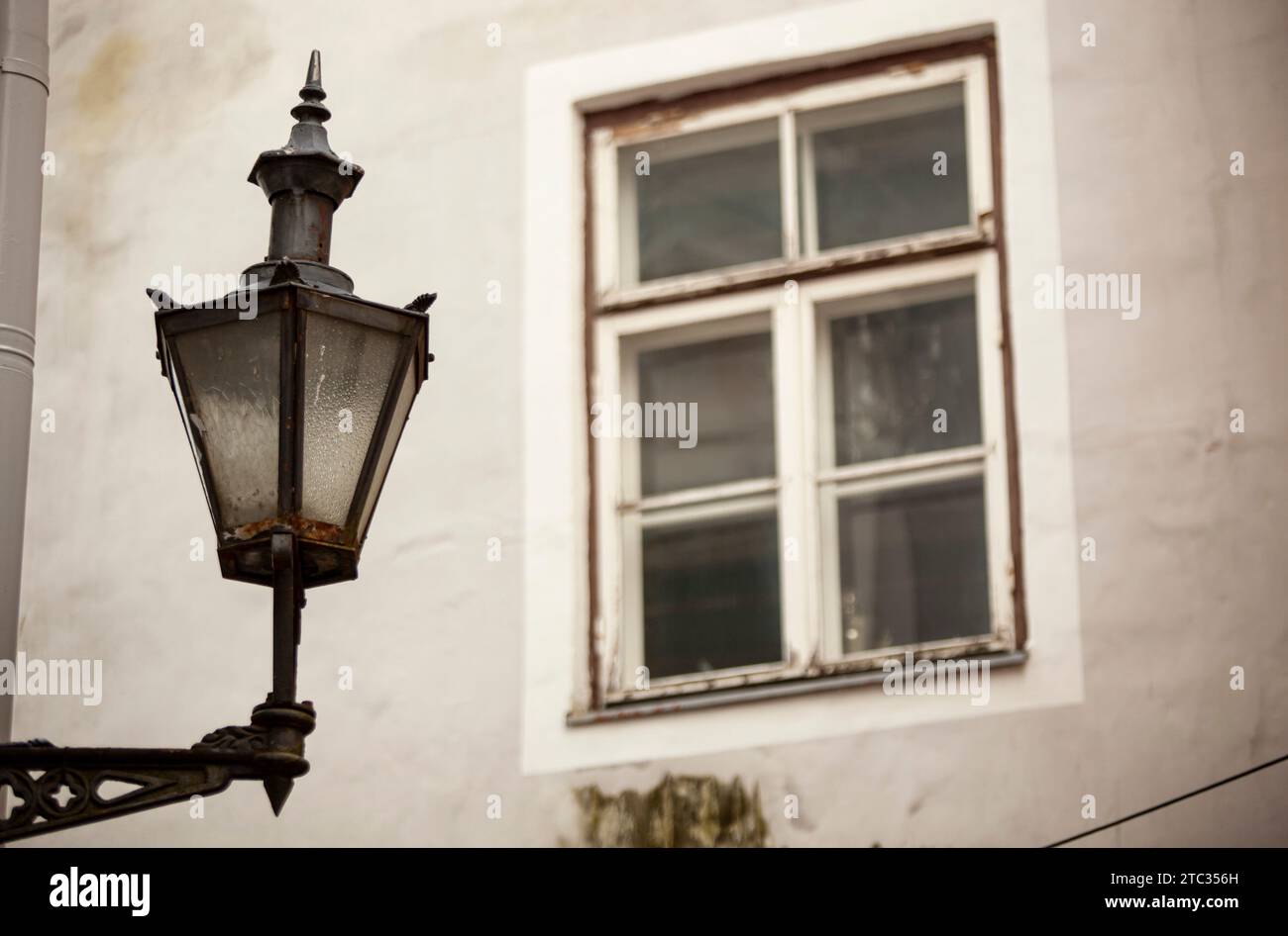 Un vieux lampadaire sombre avec des inserts en verre est accroché au mur d'une maison avec une fenêtre en bois sombre à Tallinn. Photo de haute qualité Banque D'Images