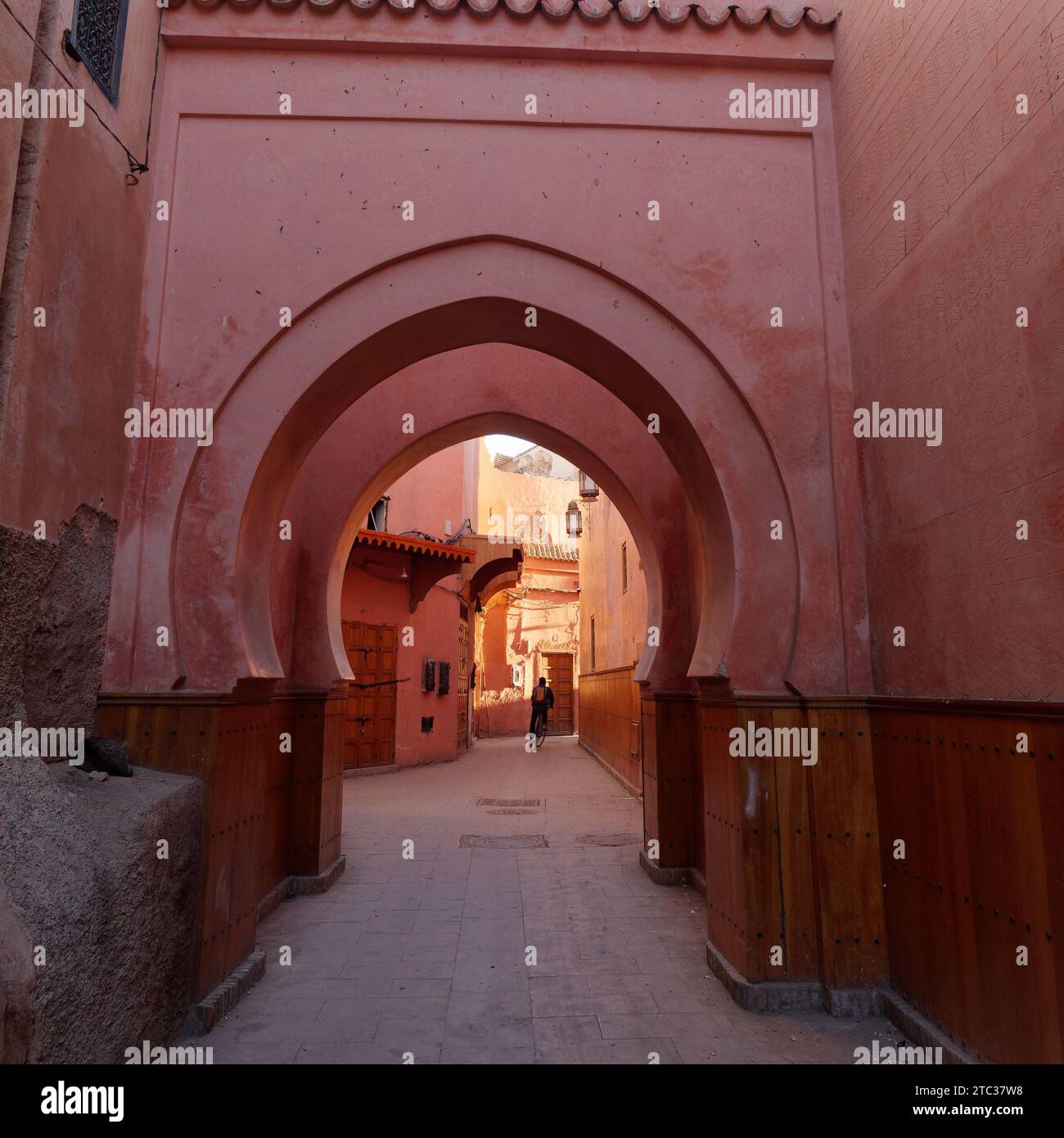 Les cyclistes passent par des arcades dans une rue étroite de la médina de Marrakech aka Marrakech avec la mosquée au loin, Maroc, 10 décembre 2023 Banque D'Images