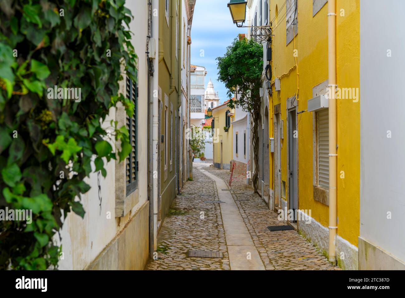 Une étroite ruelle résidentielle pavée dans la vieille ville historique de Cascais, Portugal, avec la tour de l'église notre-Dame des navigateurs en vue. Banque D'Images