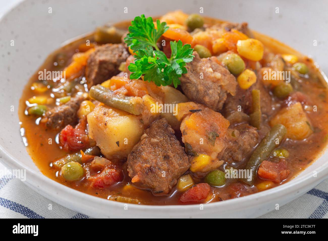 Ragoût de bœuf aux légumes avec pommes de terre, haricots verts, carottes, céleri, pois et maïs, dans un bol gris, horizontal, gros plan Banque D'Images