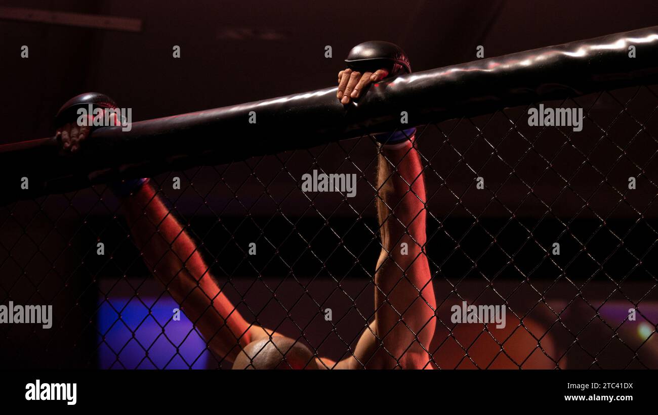 mma Fighter accroché au sommet du mur octogonal avec sa tête vers le bas intense contemplation MMA Fighter pause Banque D'Images