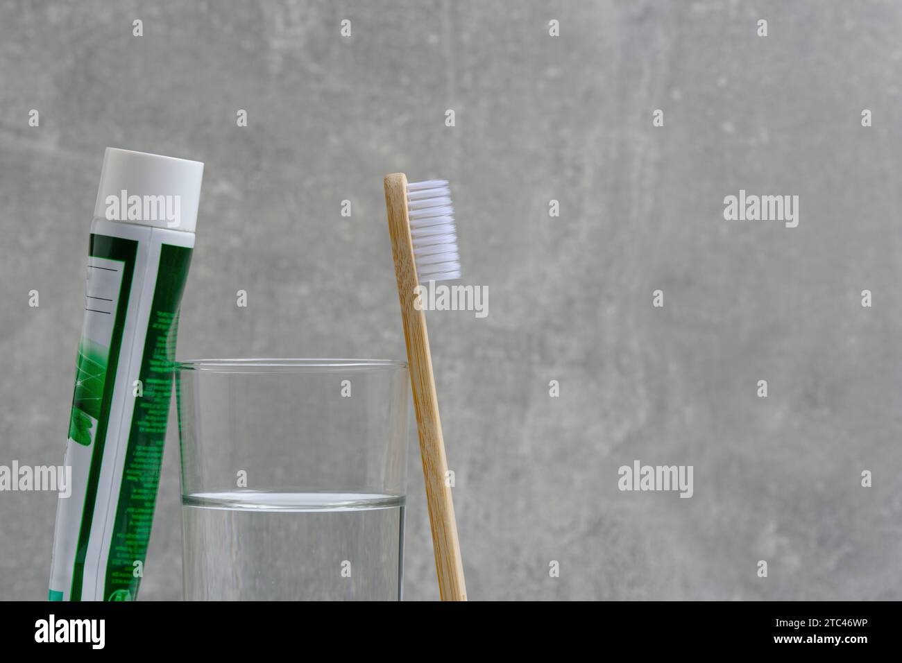 Tube dentifrice, brosse et fond gris eau en verre dans la salle de bain Banque D'Images