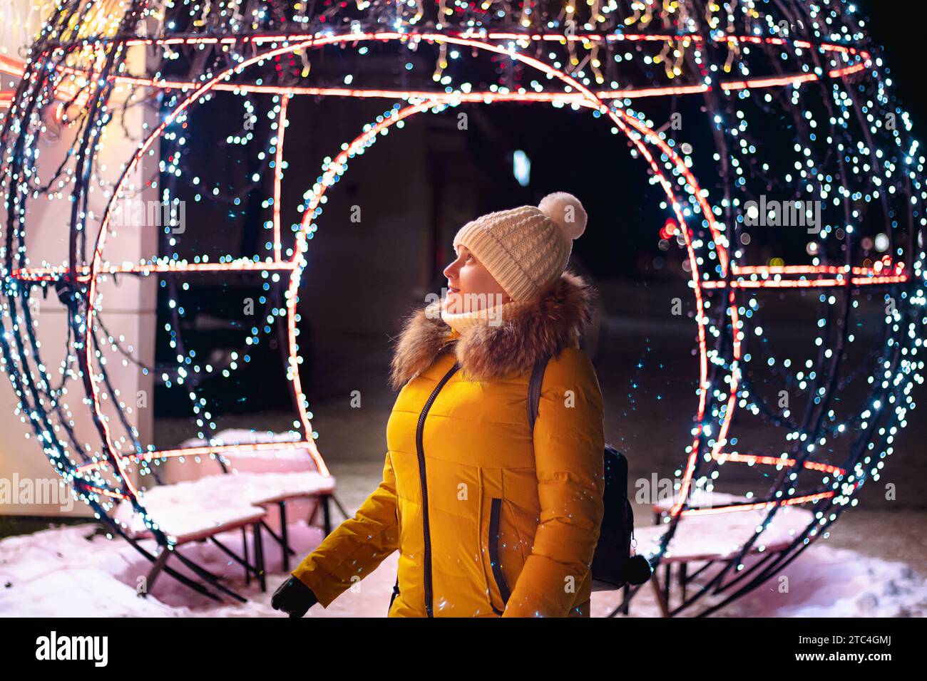 Jeune femme touriste dans le chapeau tricoté regarde les décorations festives de la ville de Noël. Marché de Noël, veilleuses. Banque D'Images