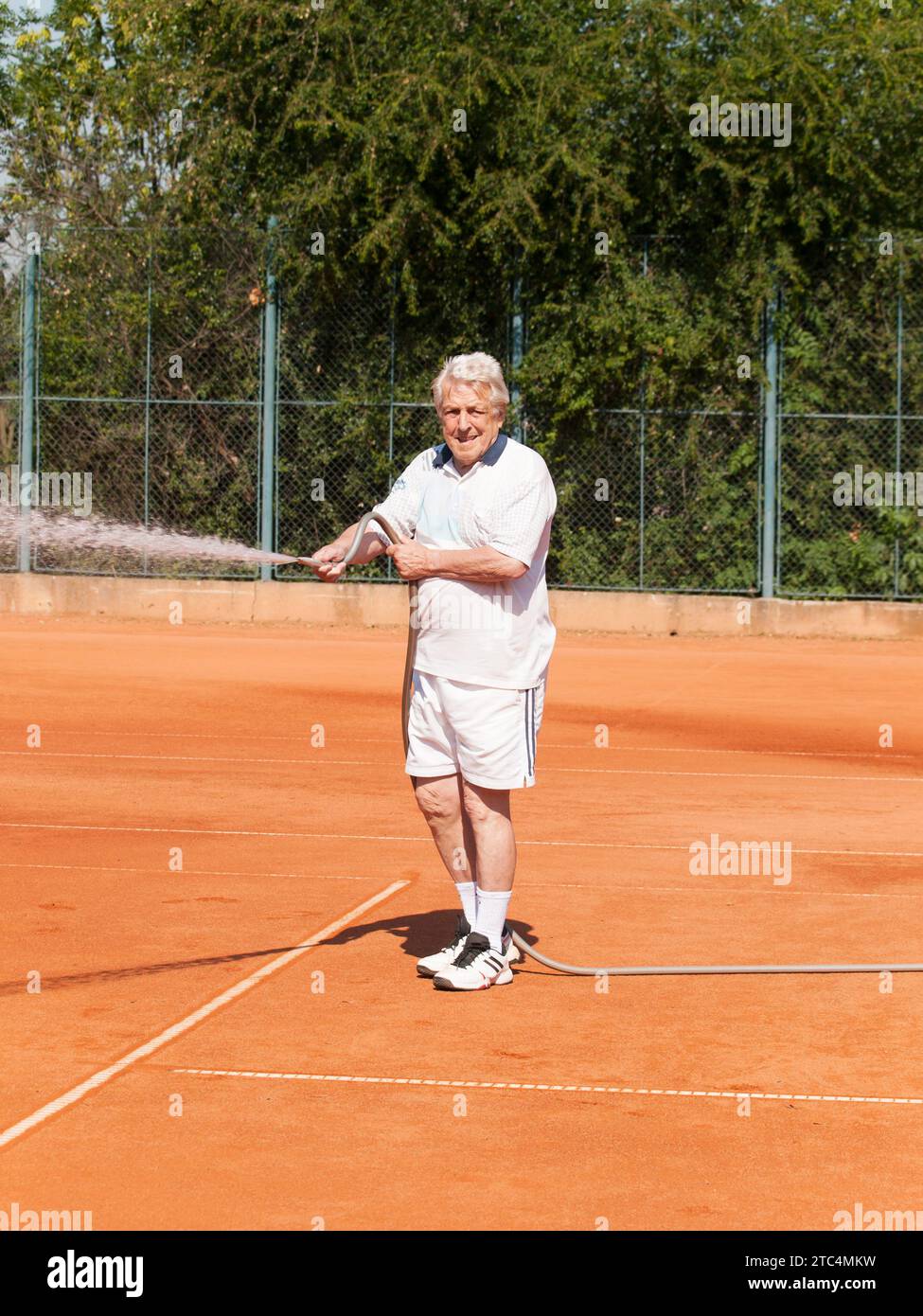 Les hommes âgés arroslig court de tennis avant de jouer Banque D'Images