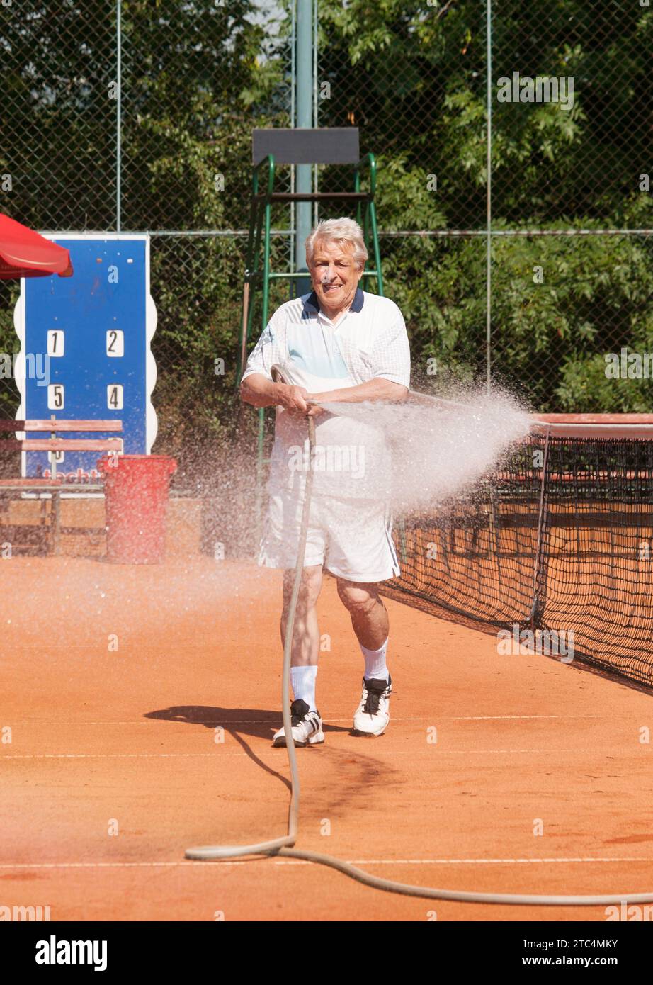 Hommes seniors arrosant le court de tennis avant de jouer Banque D'Images