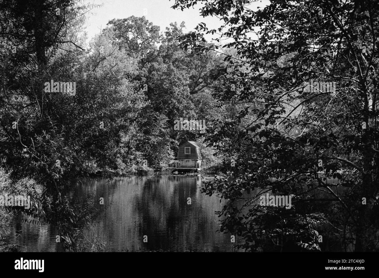 Concord, Massachusetts - Un ancien hangar à bateaux historique se dresse sur la rive de la rivière Concord, entouré d'arbres luxuriants en été sous le soleil de l'après-midi. Image Banque D'Images