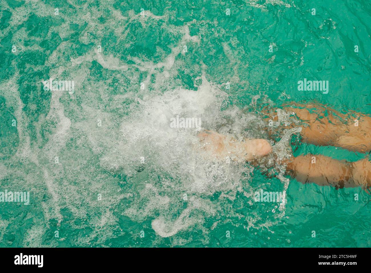 Jambes d'homme dans la piscine. Vue de dessus de la partie inférieure du corps de l'homme nageant dans l'eau bleue. Les pieds éclaboussent dans la piscine. Vacances et Banque D'Images