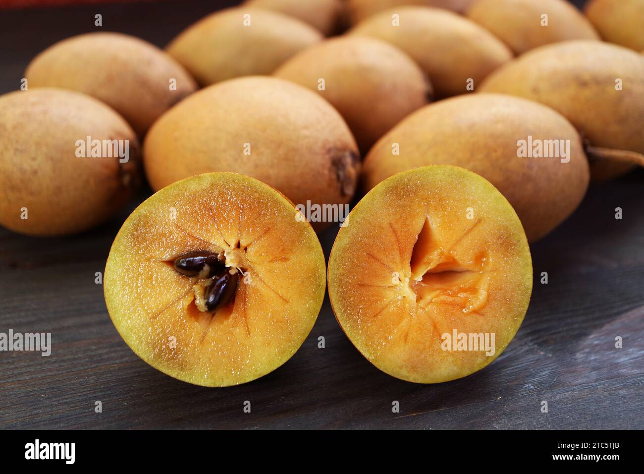 Gros plan de fruits coupés Sapodilla avec tas de fruits entiers en toile de fond Banque D'Images