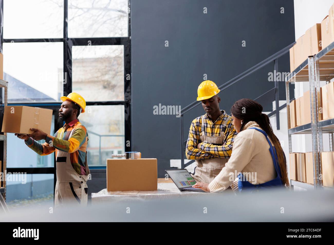 Gestionnaires d'entrepôt afro-américains discutant du ticket de pick sur ordinateur portable. Tous les employés de magasin de détail de commerce électronique noir travaillant dans la salle de stockage et préparant la commande de l'acheteur pour la dipatching Banque D'Images