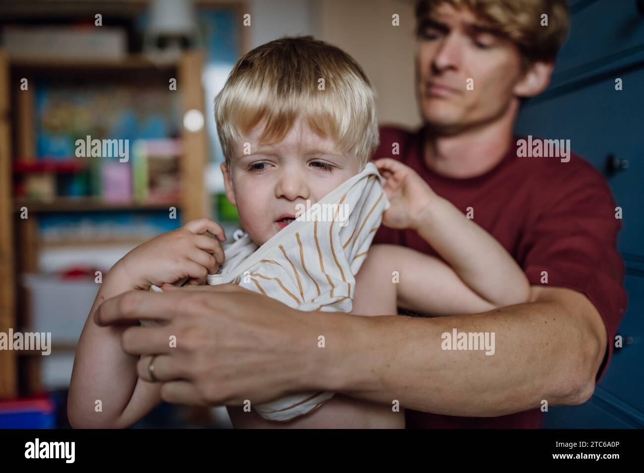 Père mettant la chemise sur le petit fils, changeant de pyjama le matin. Garçon est triste, pleurant. Banque D'Images