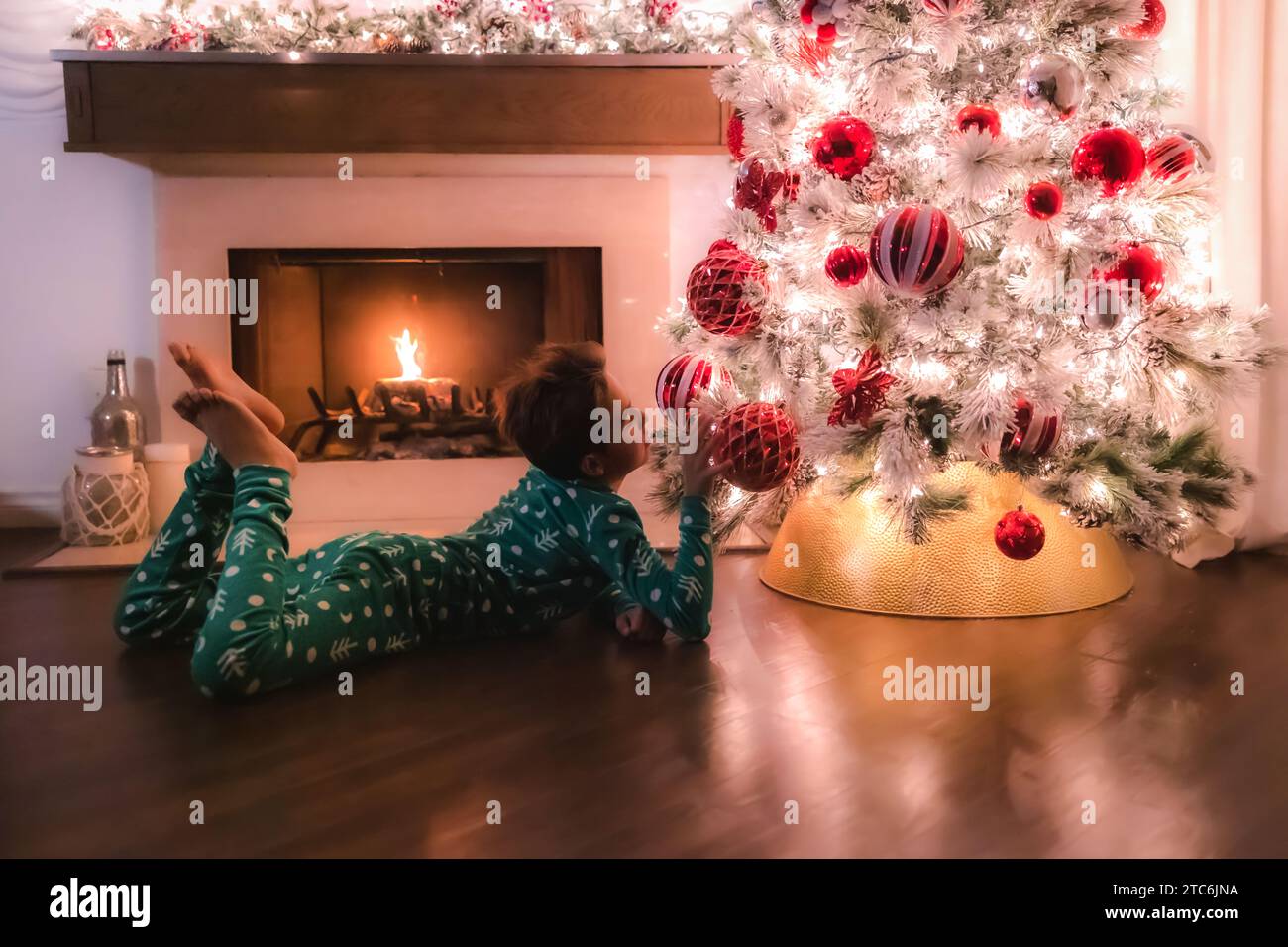 Garçon en pyjama couché à côté d'un arbre de noël avec cheminée Banque D'Images