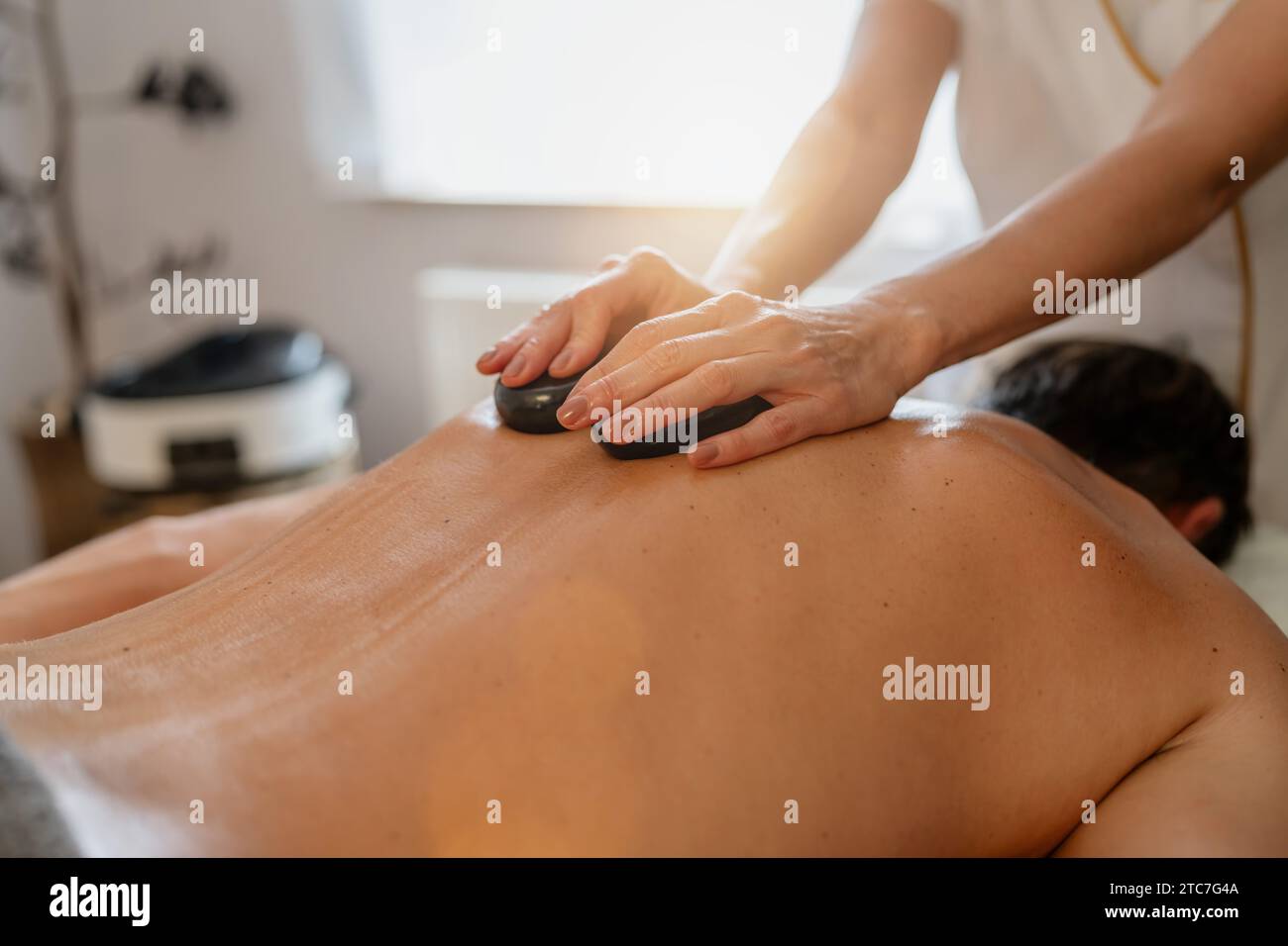 Thérapeute donnant un massage aux pierres chaudes à un client allongé face cachée Banque D'Images