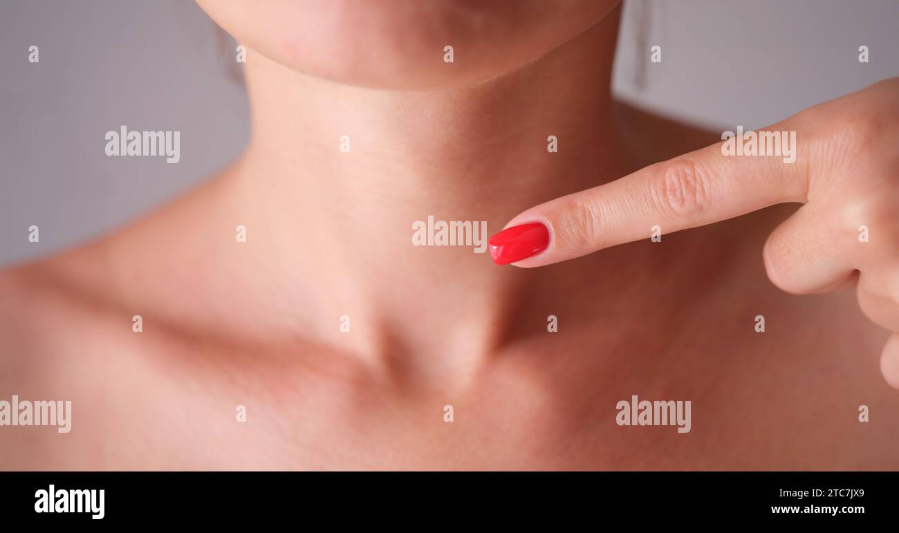 Femme avec une manucure rouge pointant le doigt sur la zone du cou avec la glande thyroïde gros plan Banque D'Images