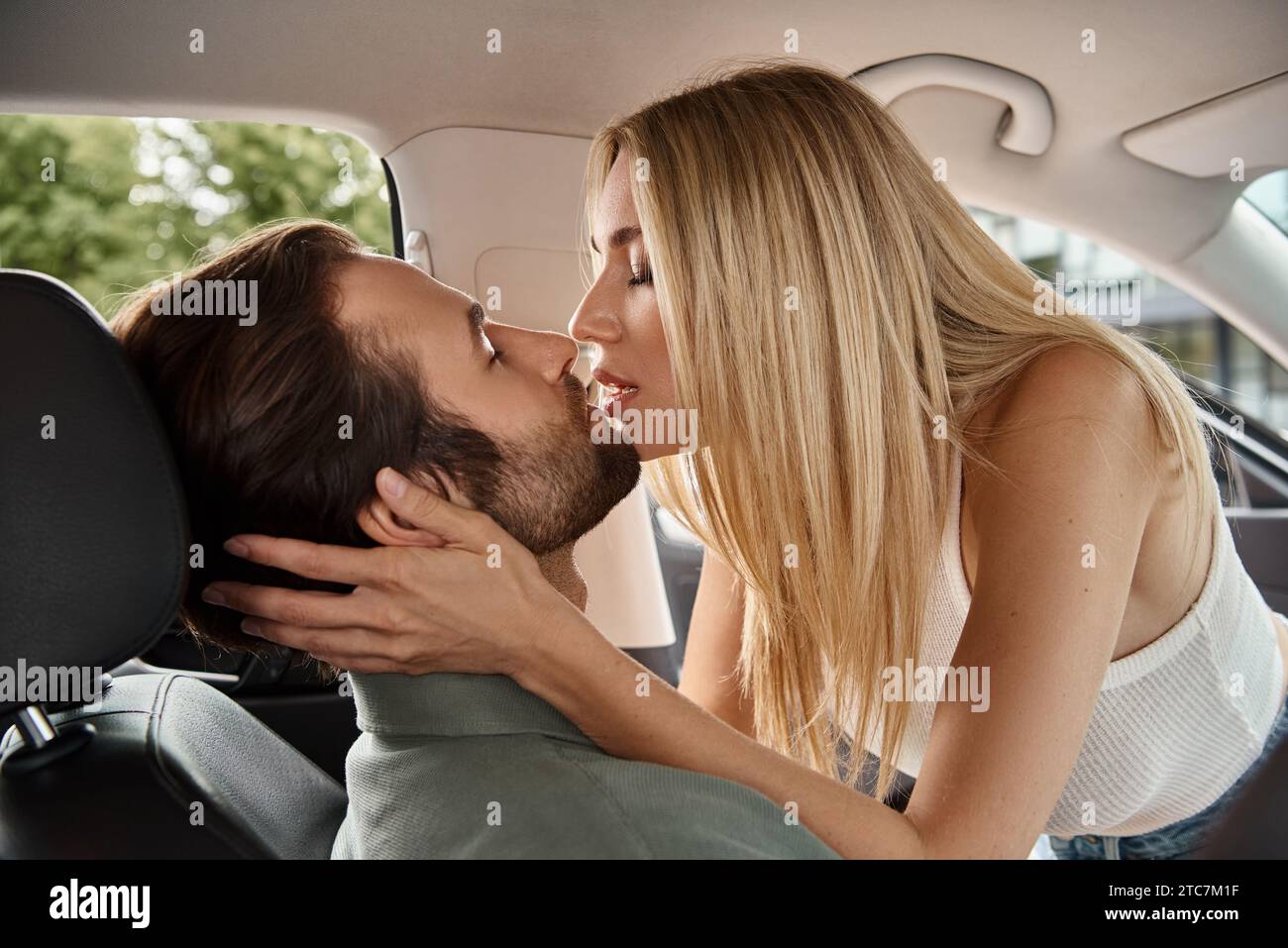 femme blonde attrayante avec les yeux fermés embrassant l'homme sur le siège des conducteurs dans la voiture moderne, histoire d'amour Banque D'Images