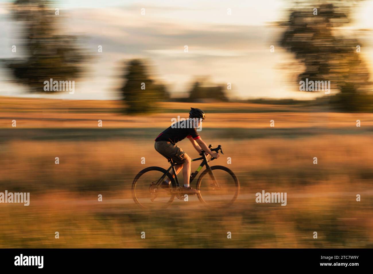 Cycliste sur un vélo de gravier dans un champ au coucher du soleil. Effet de flou de mouvement. Concept de voyage et de mode de vie actif. Banque D'Images