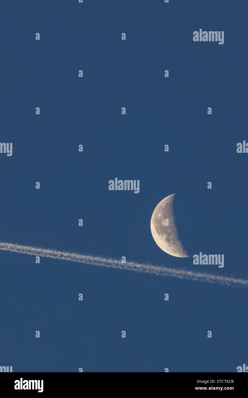 Une belle image d'une demi-lune et d'une traînée de condensation brillante à l'aube par un matin clair d'hiver au Royaume-Uni Banque D'Images