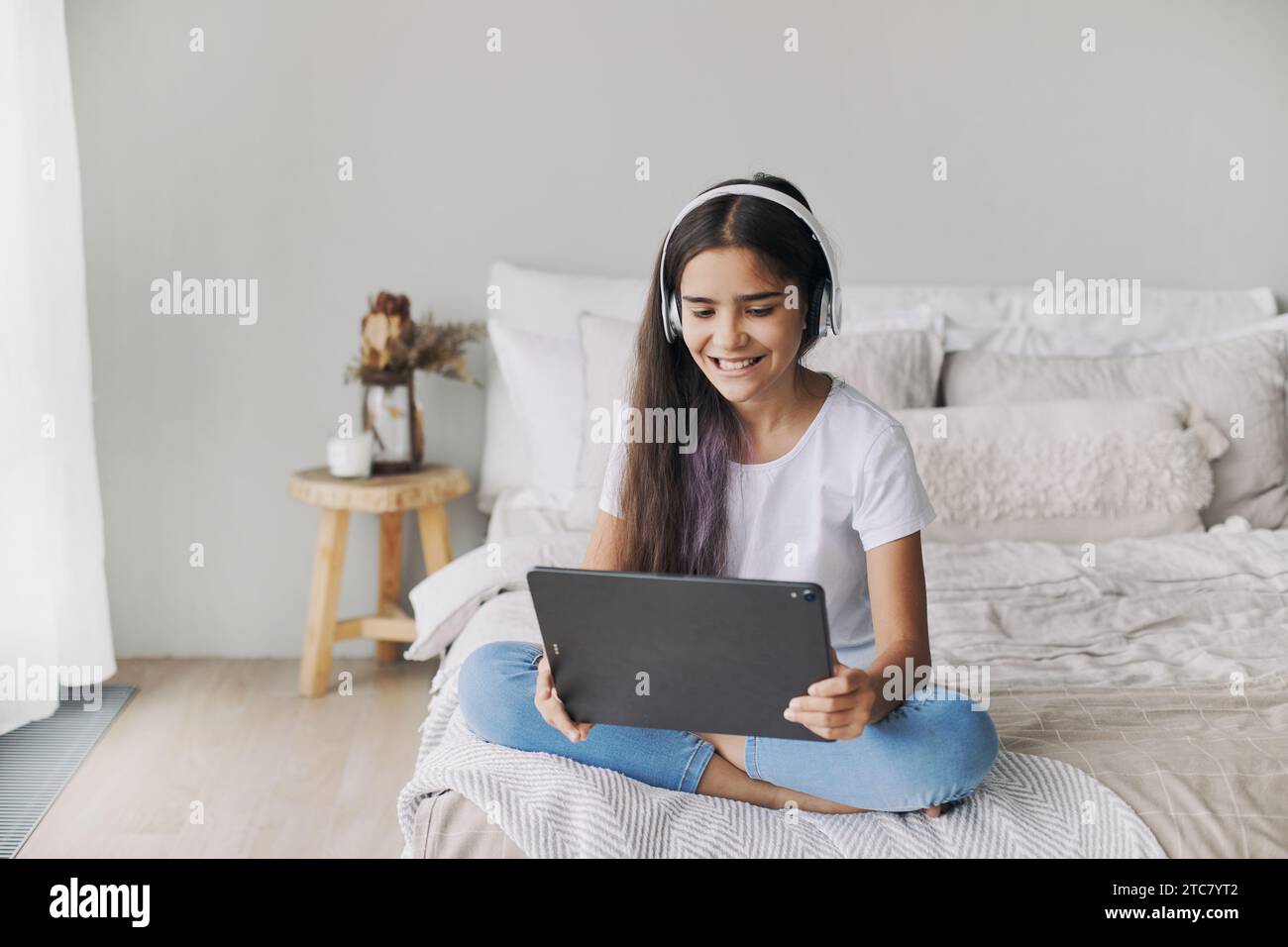 Attrayant pré-adolescent fille des années 12 portent des écouteurs sans fil en utilisant la tablette numérique moderne assis sur le lit dans la chambre confortable. I génération et utilisation des technologies f Banque D'Images