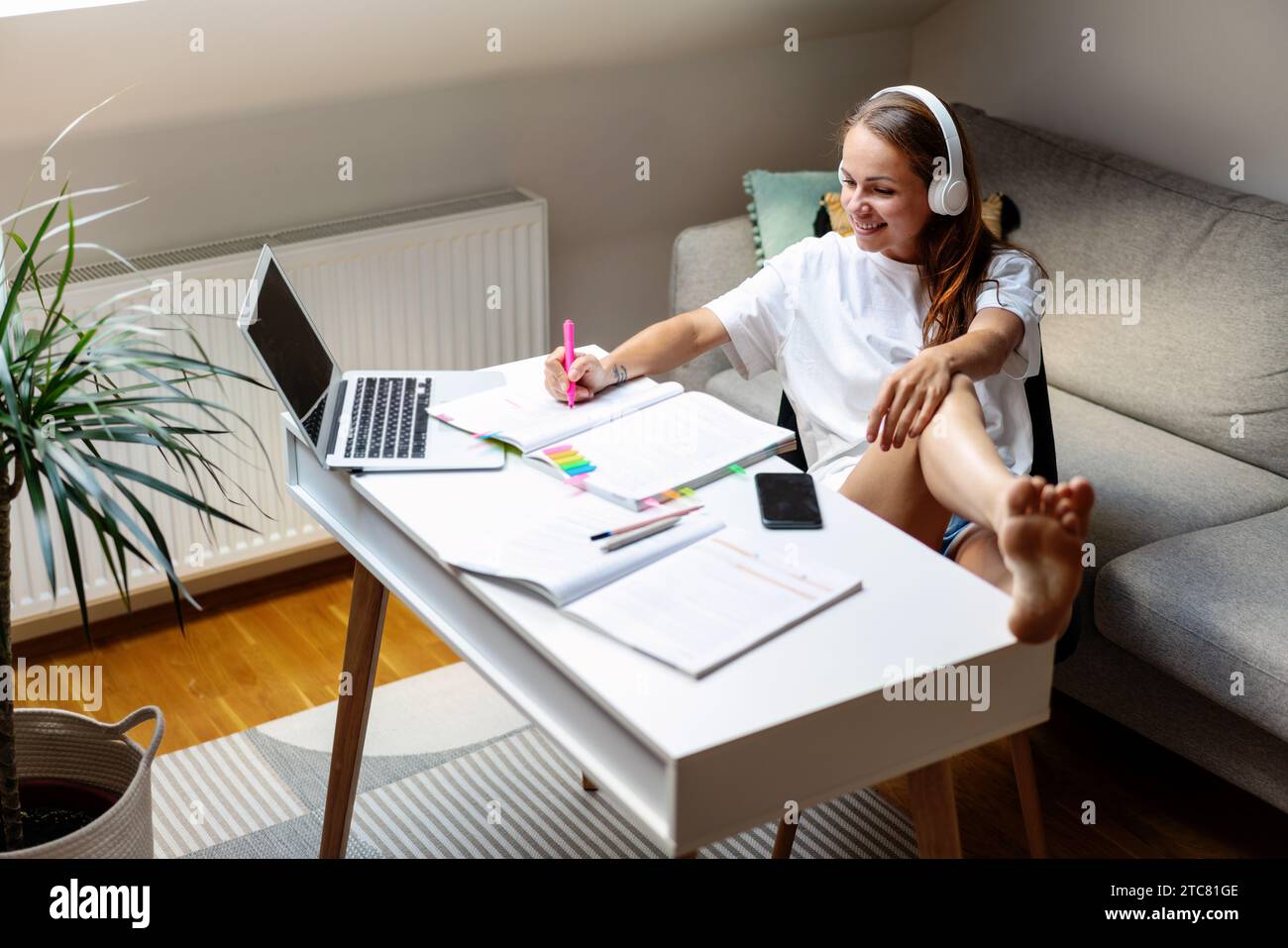 Éducation à domicile. Femme brune attrayante dans les écouteurs en utilisant le cahier de travail au bureau à la maison. Utilisation d'un ordinateur portable pour l'e-learning. Banque D'Images