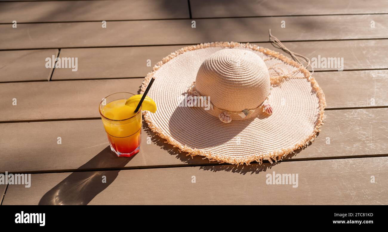 Cocktail d'été avec chapeau de paille sur une terrasse en bois, symbolisant la détente et les vibrations de vacances Banque D'Images
