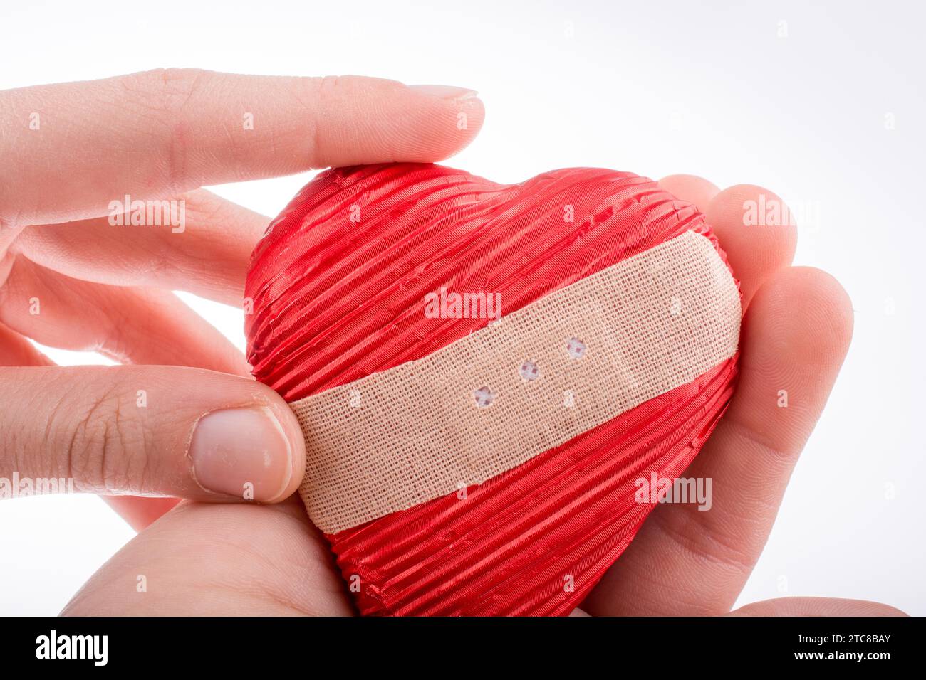 Main tenant un coeur blessé avec plâtre à la main sur fond blanc Banque D'Images