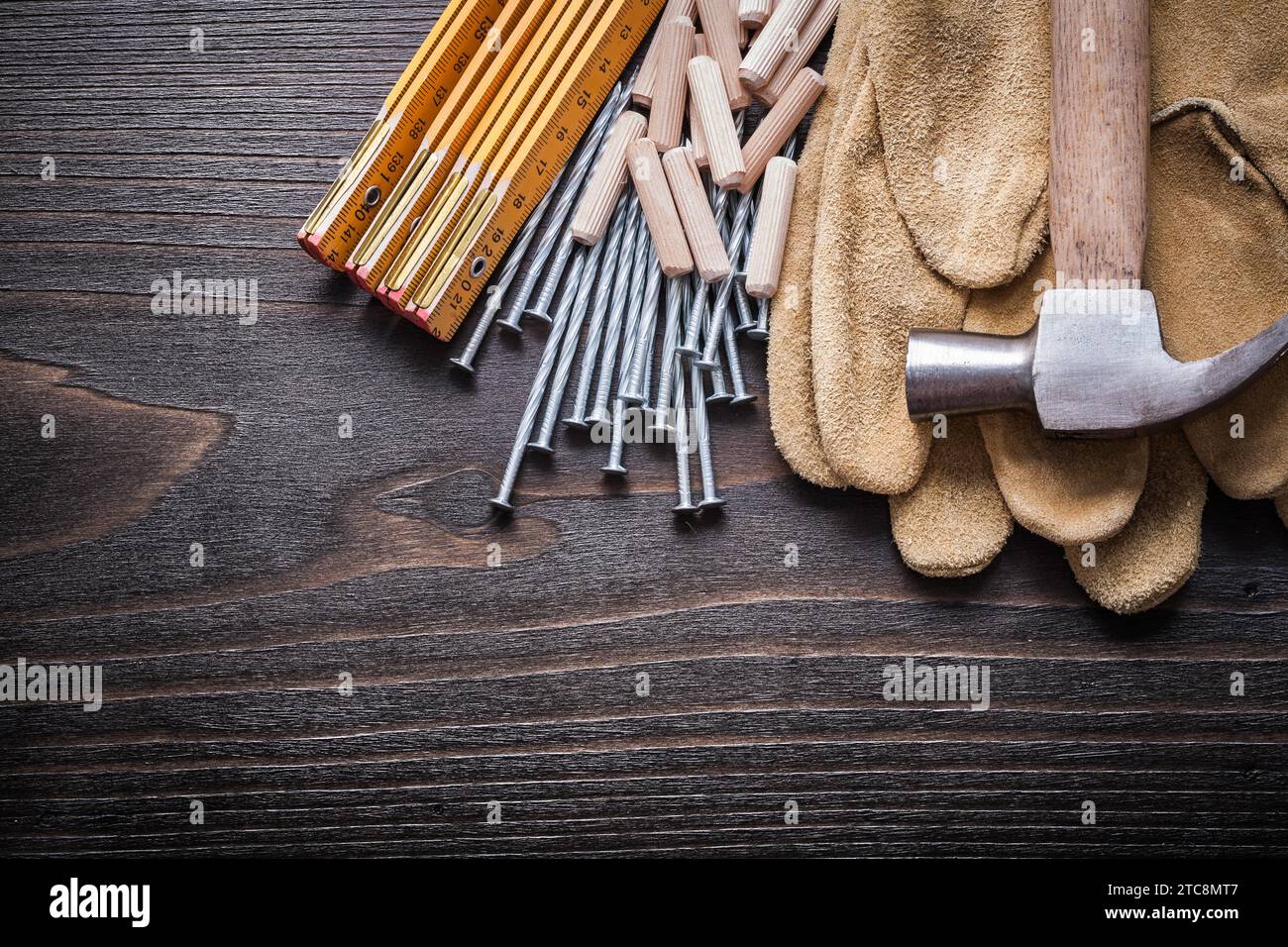 Pile de mètre en bois de chevilles pince marteau gants de sécurité bruns et clous en métal sur le concept de construction de panneau de bois vintage Banque D'Images