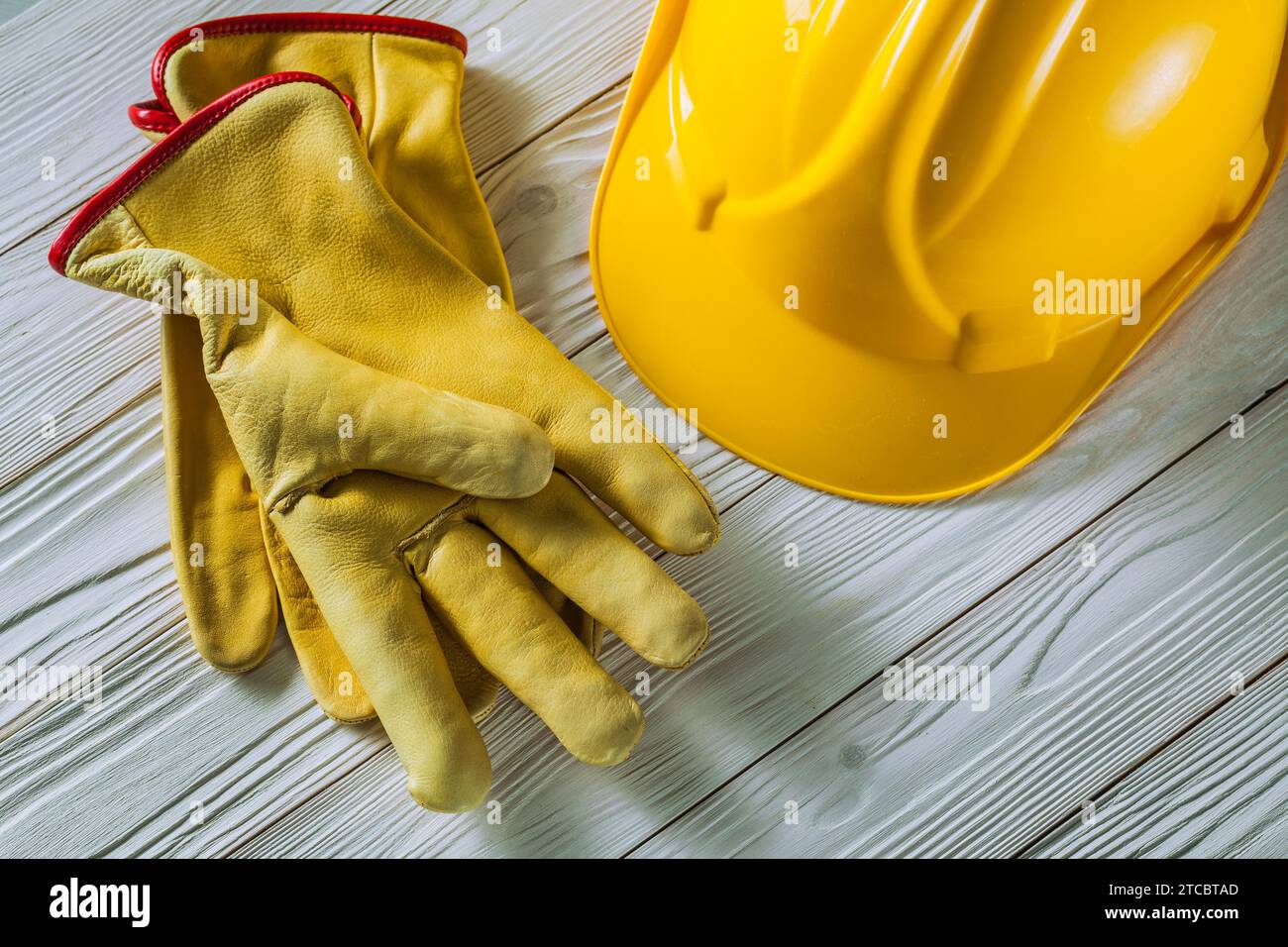 Gants de travail en cuir jaune et casque de construction sur vieux panneaux en bois laqué blanc Banque D'Images