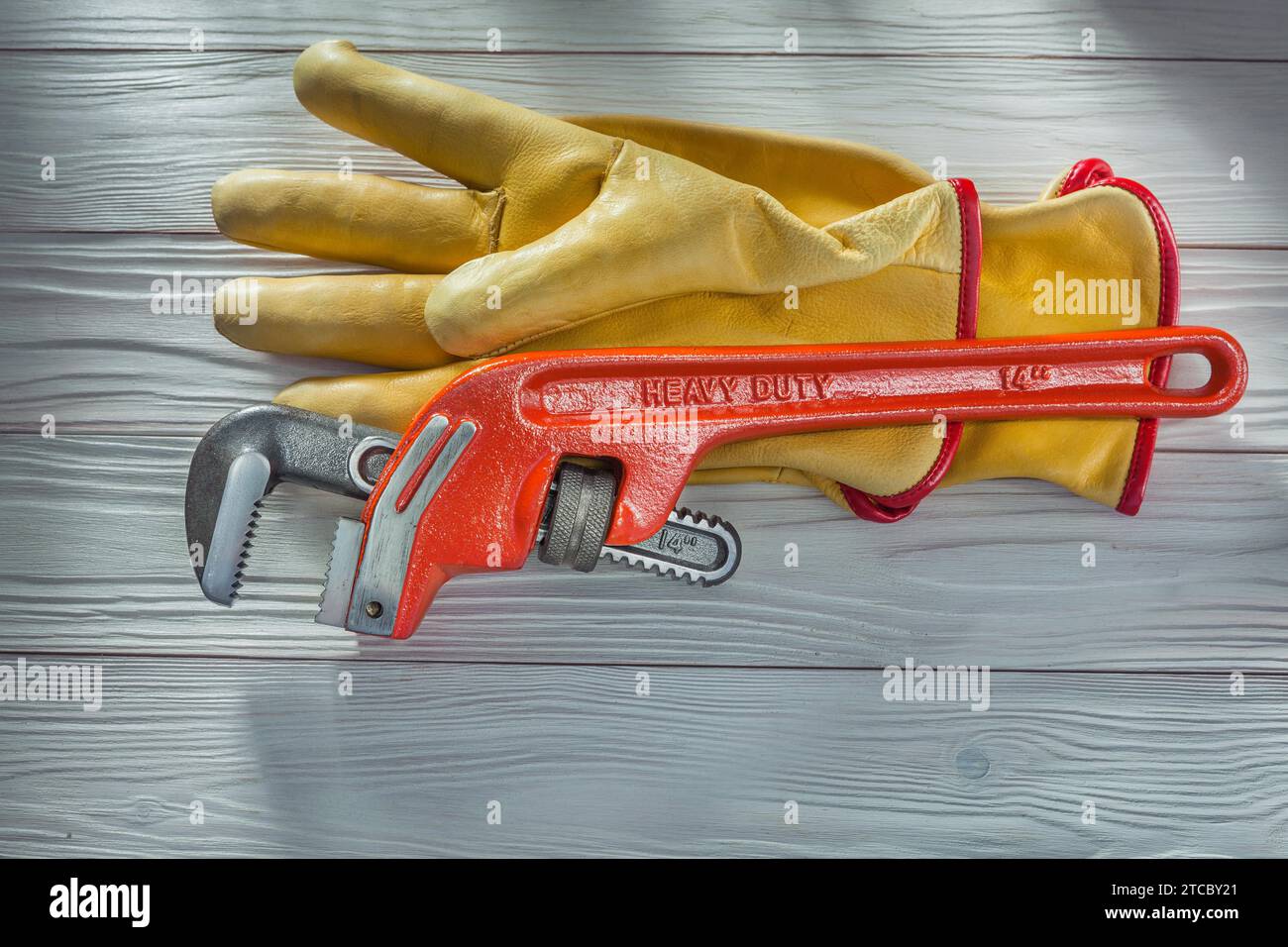 Clé singe de plombier et gants de travail en cuir jaune sur panneaux en bois laqué blanc vintage Banque D'Images